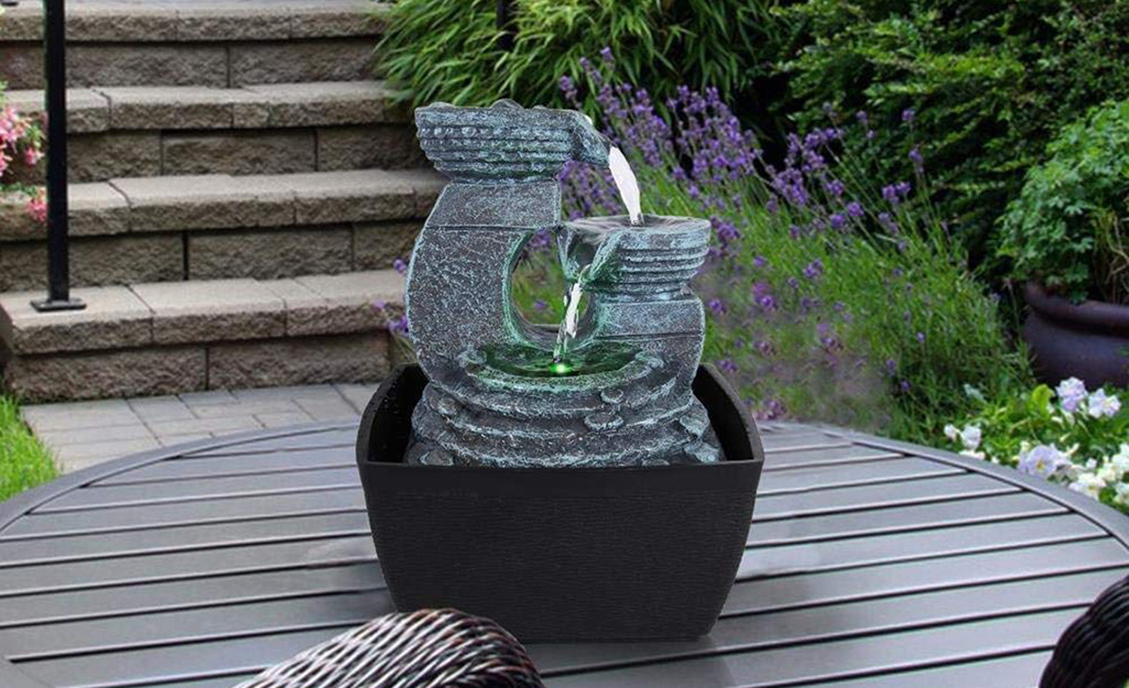 A tabletop fountain on an outdoor table on a patio.