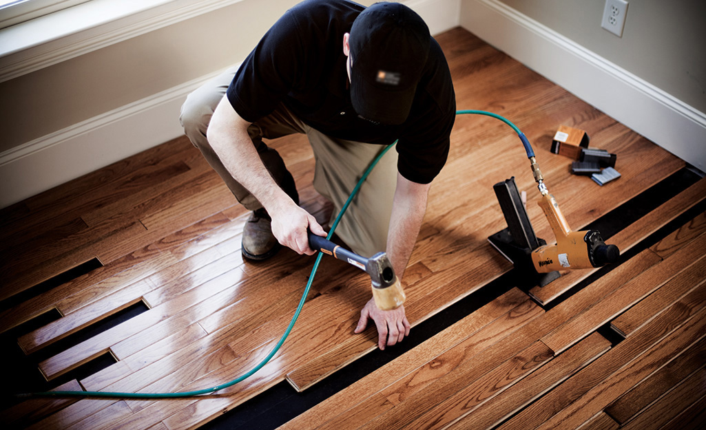A person installs strips of hardwood flooring in a room.    
