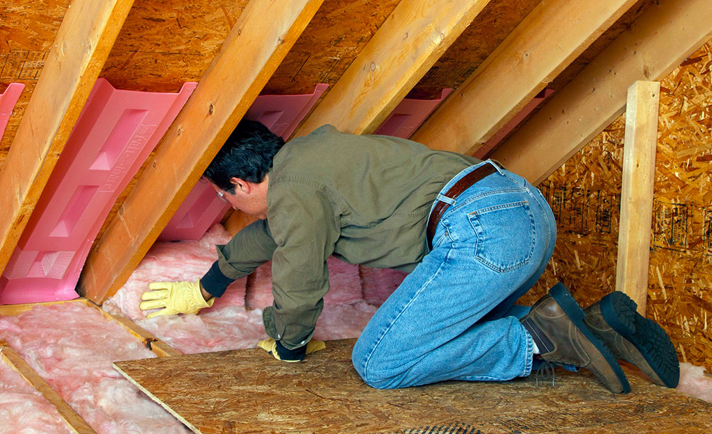 A man installs insulation in an attic.