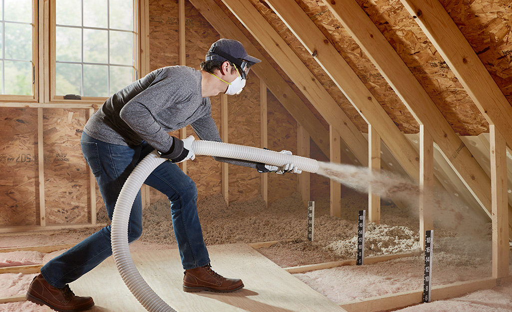 A man sprays loose insulation in an attic.