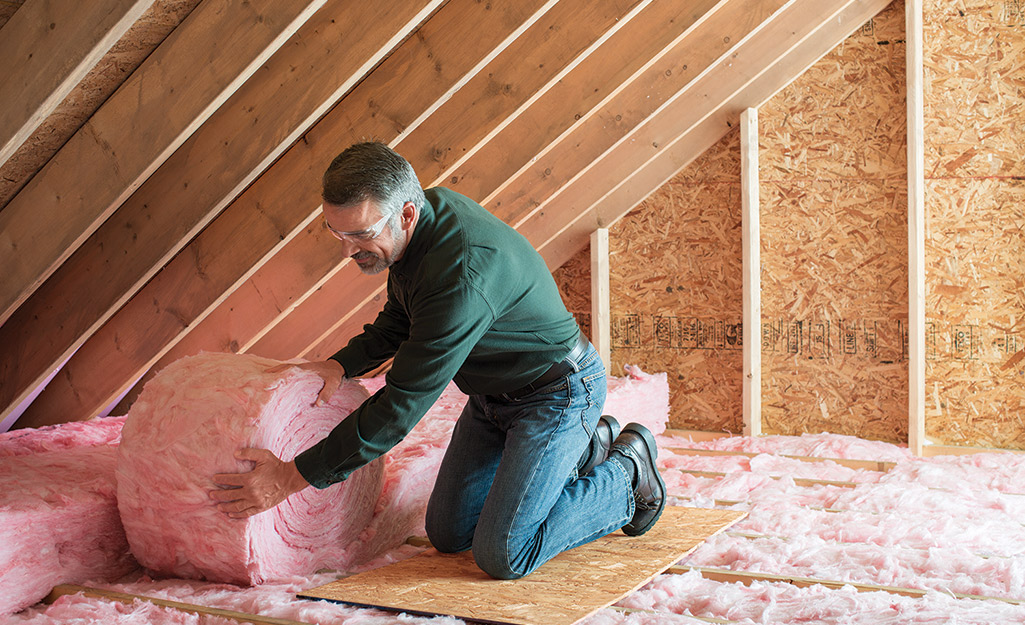 A man installs rolled insulation in an attic.