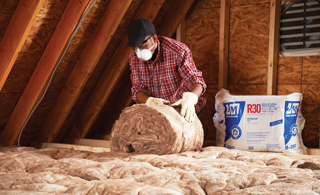 A person installing rolled insulation in an attic.
