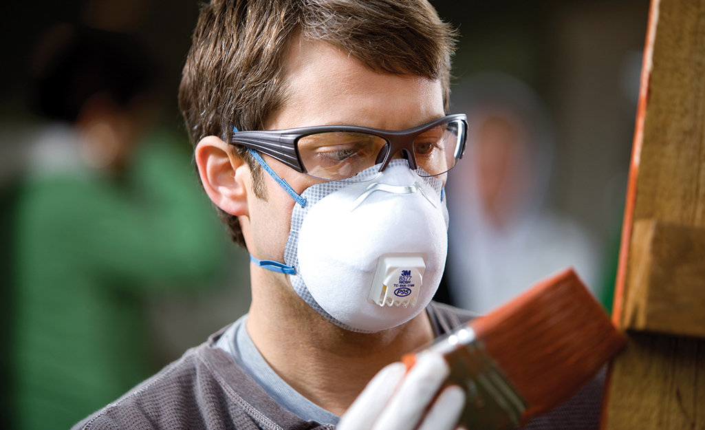 A man wearing a respirator while staining wood.