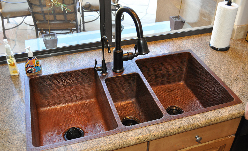 A triple bowl kitchen sink featuring a copper finish.