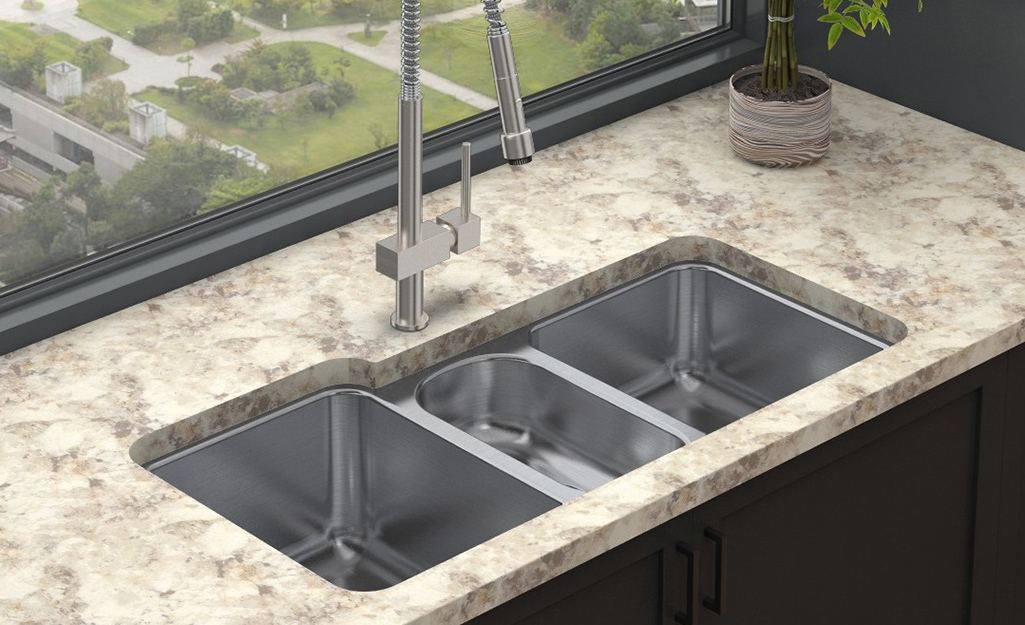 A triple bowl sink in a kitchen with granite countertops.