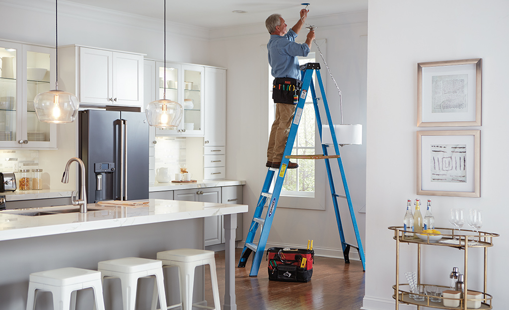 A man standing on a step ladder to paint a kitchen ceiling.