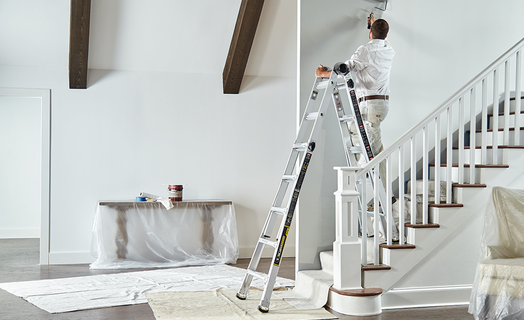 A man standing on a multi-position ladder placed on stairs.