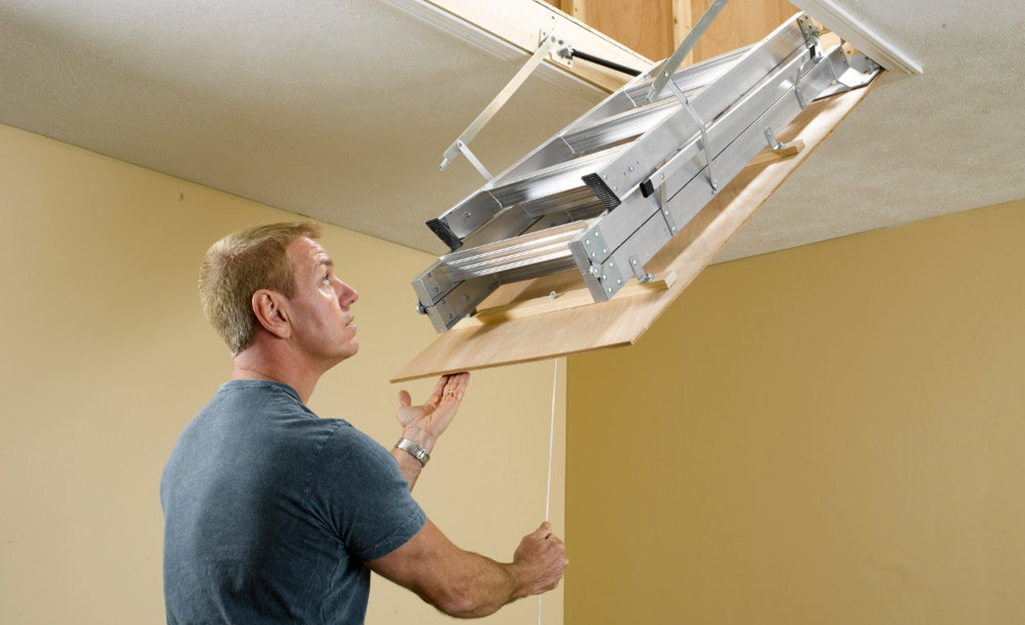 A man pulling down an attic ladder.