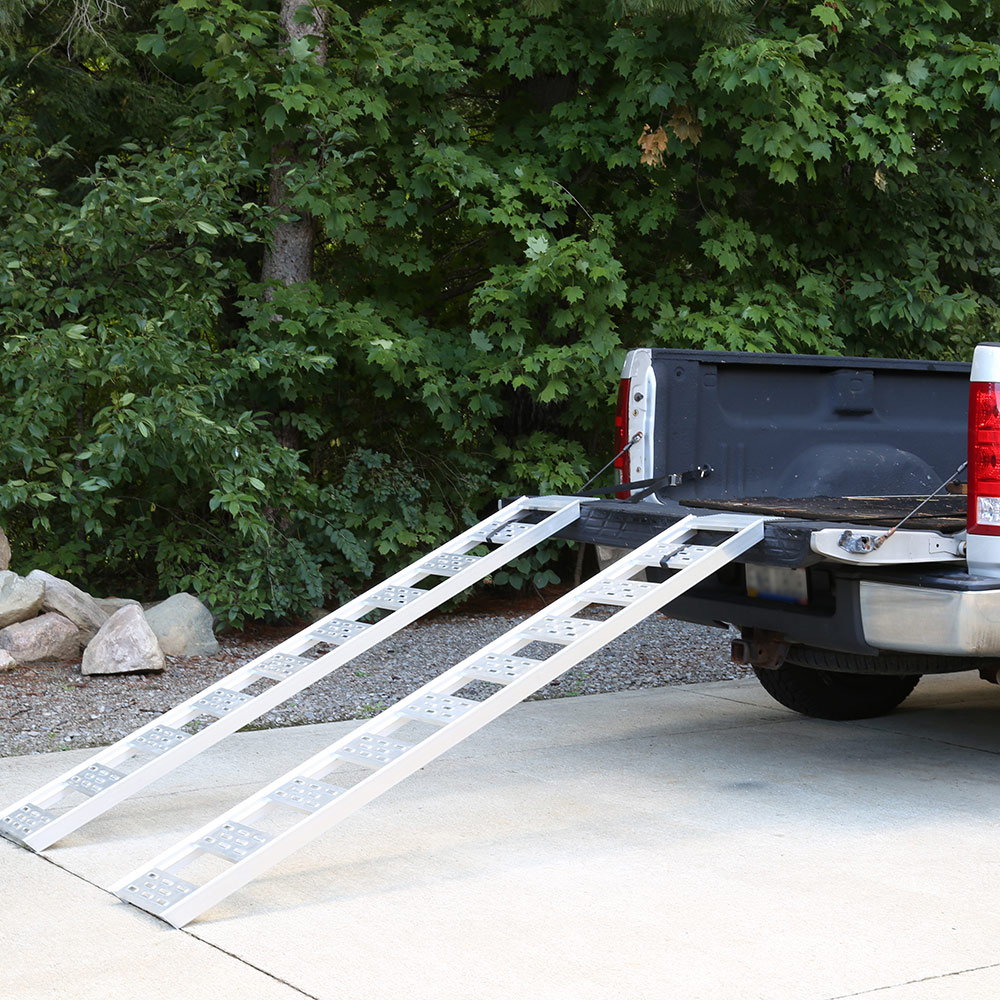 A loading ramp extends from the ground into the bed of a pickup truck.