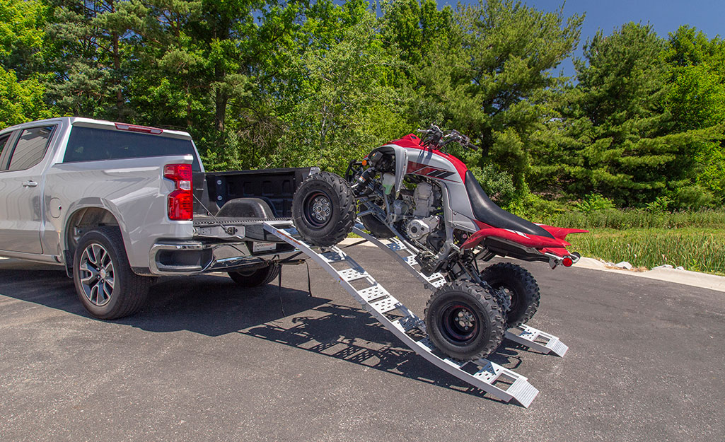 An ATV rests on a loading ramp while being loaded into the back of pickup truck.