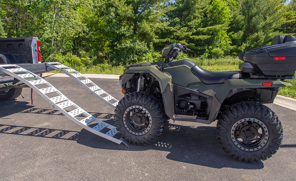 The front wheels of an ATV touch the edges of a truck loading ramp.