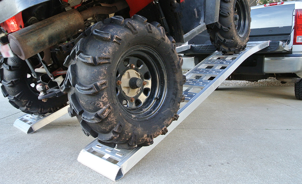 An ATV with huge tires rests on a heavy-duty truck loading ramp.