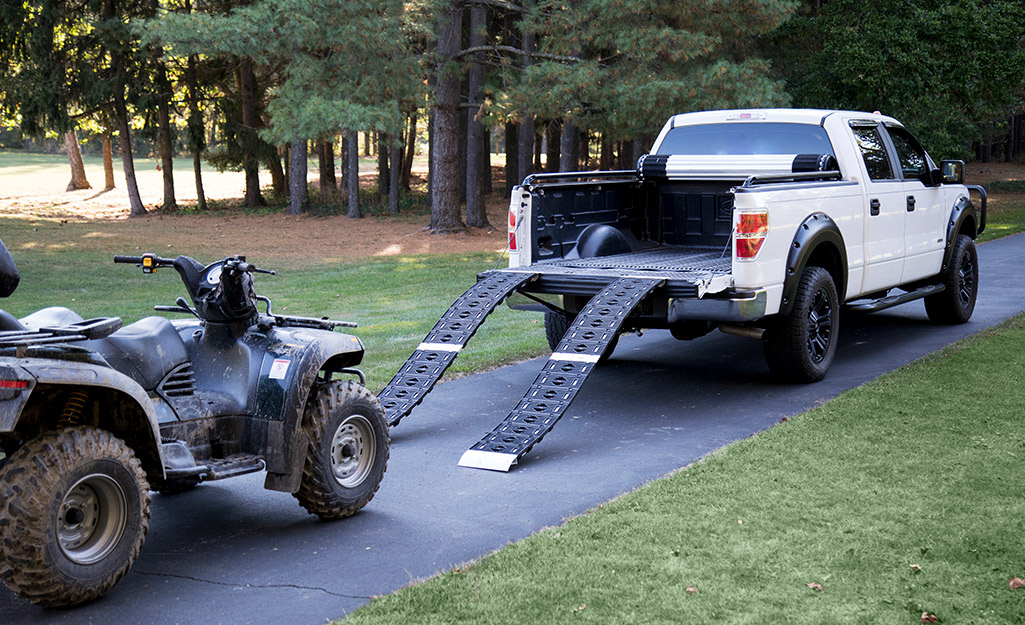 An ATV stands behind the loading ramp of a pickup truck.