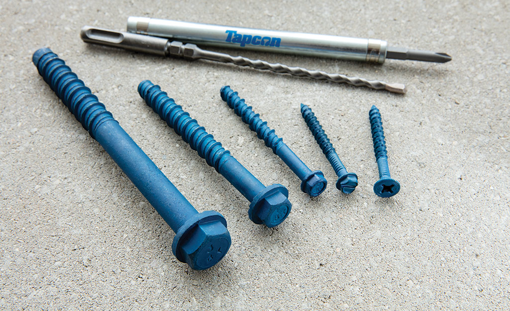 An assortment of types of concrete wall anchors lays on a concrete surface.