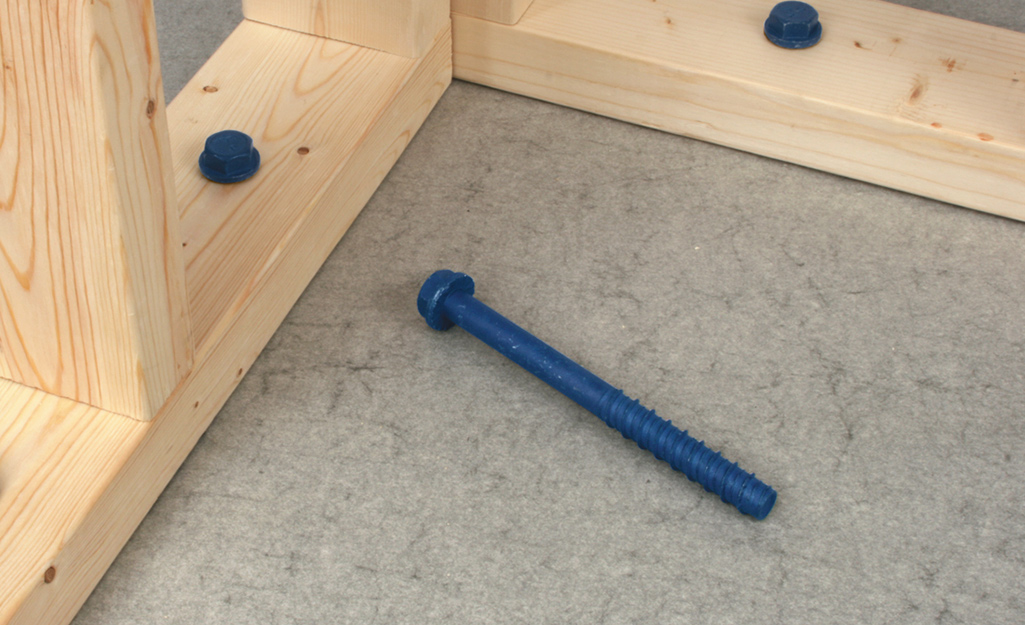 A concrete screw lays on the floor next to wood framing.