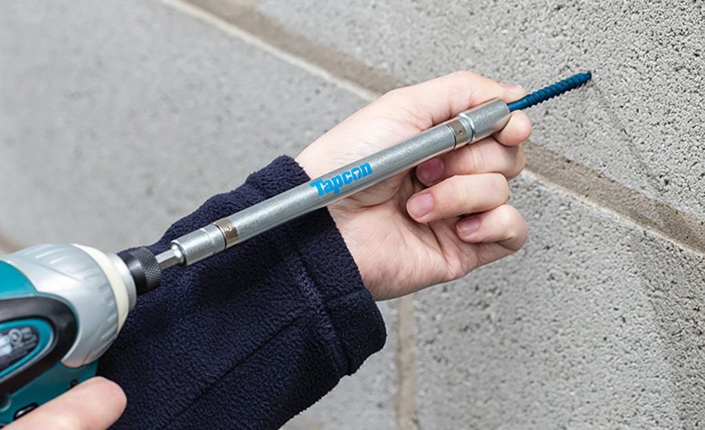 A person uses a hammer drill to insert a concrete wall anchor into a block wall.