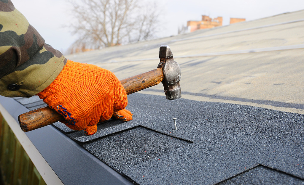 Someone hammering roofing nails into shingles.