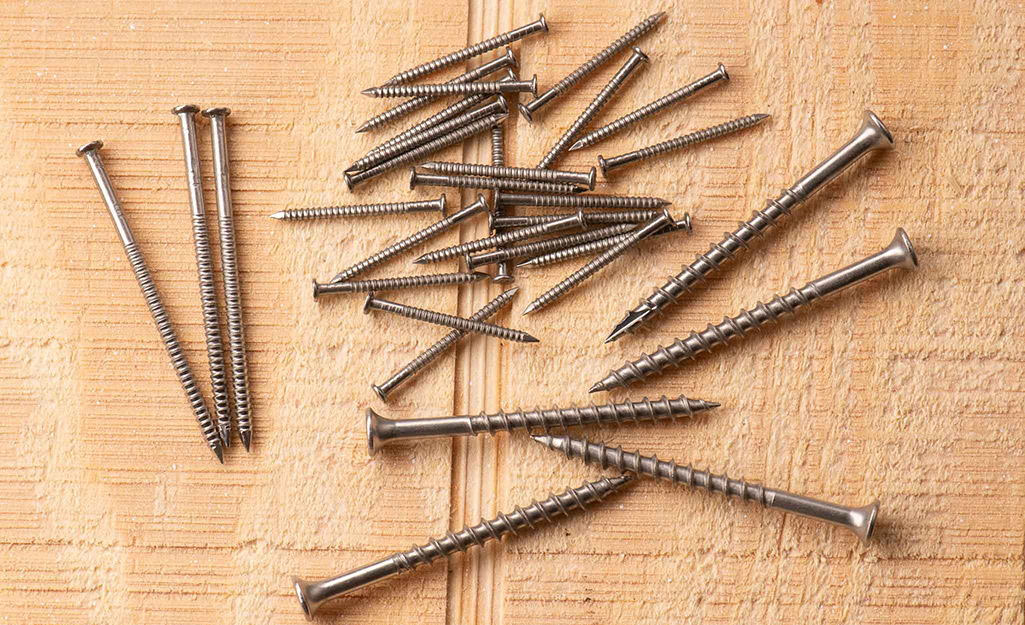 Several stainless steel screws and nails placed on a wood board.