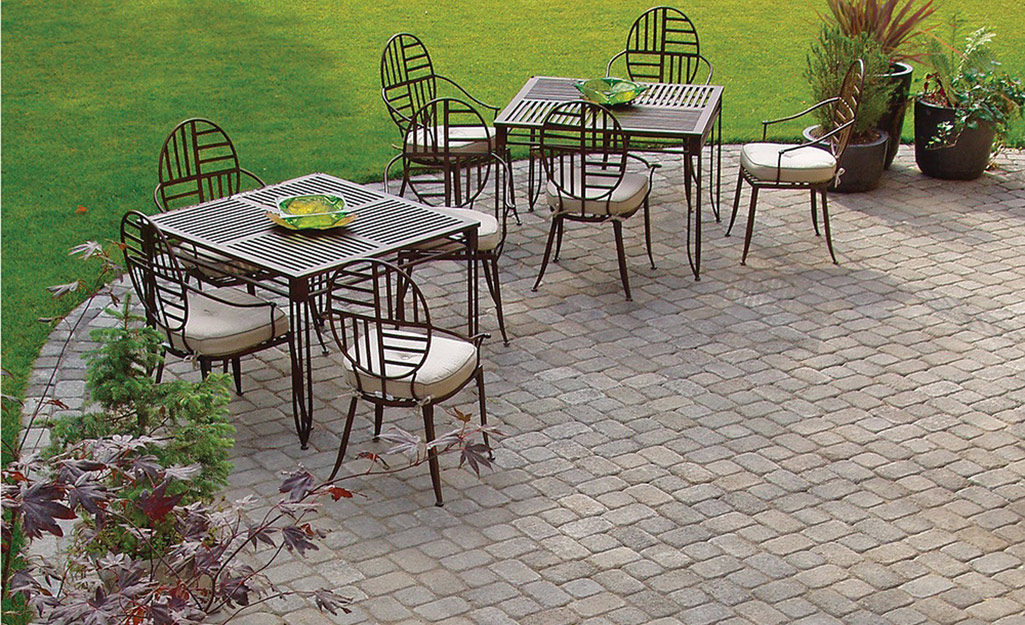 A circular paver patio with two sets of outdoor dining table and chairs surrounded by a green lawn.