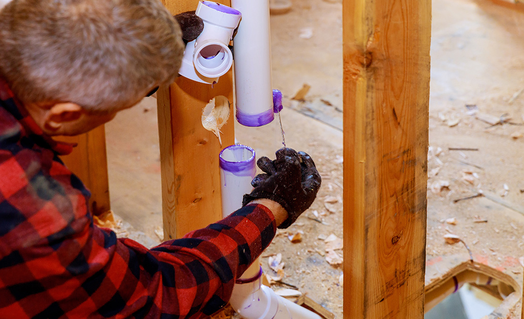 Pipe cement is being applied with a brush onto the end of a white pipe.