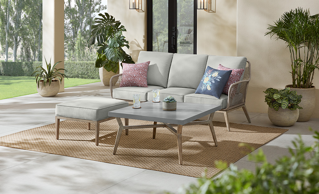 Trees and plants in containers accent a patio with a matching sofa, coffee table and ottoman.