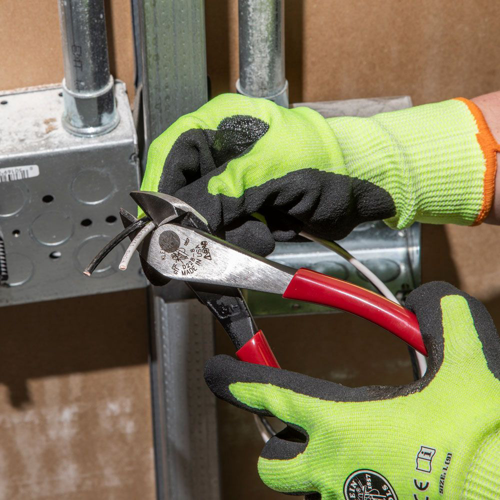 A person wearing work gloves uses pliers to cut wires near an electric box.