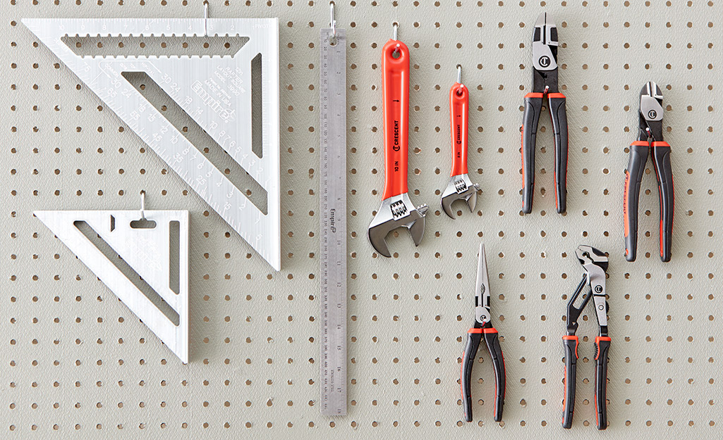 Various types of pliers hang on a peg board next to wrenches, a ruler and carpenter squares.