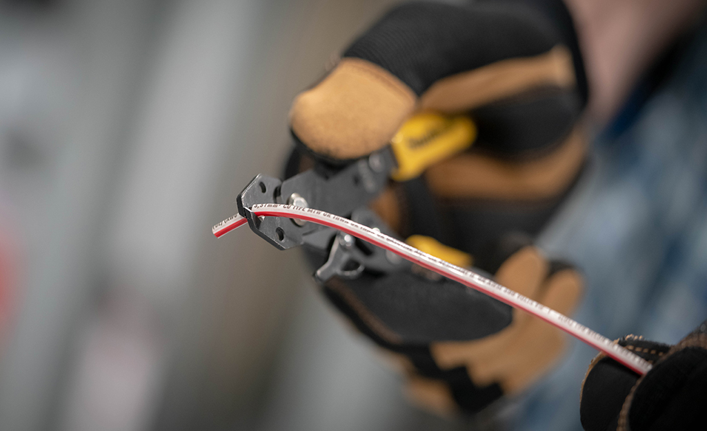 A person wearing work gloves uses a pair of wire strippers.
