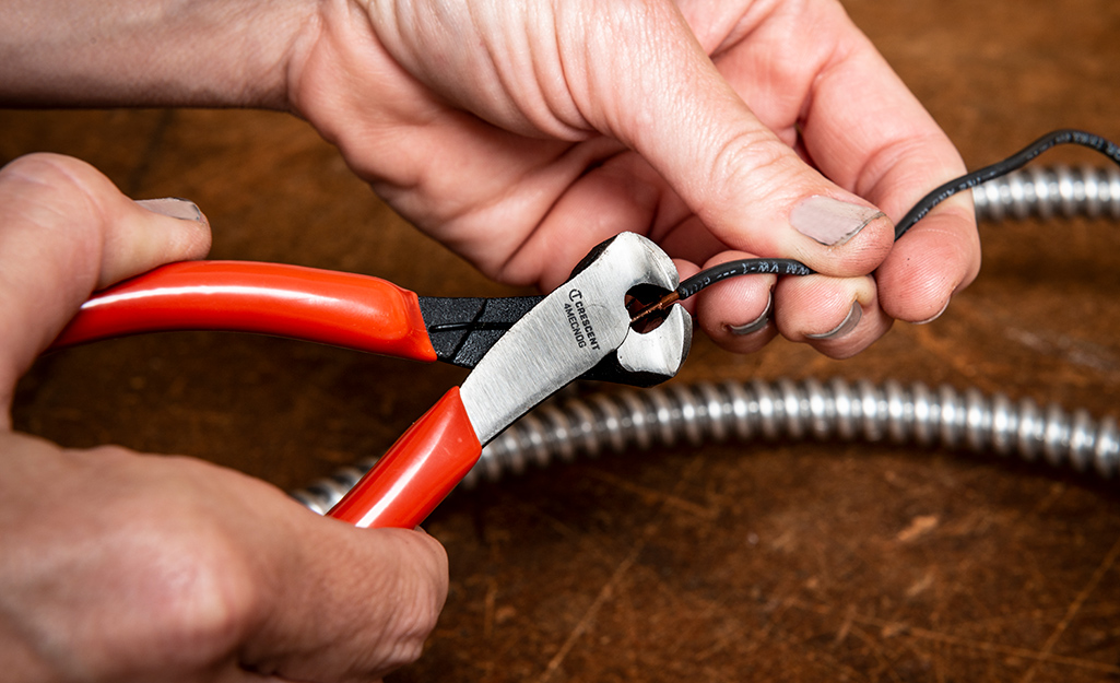 A person uses a pair of cutting pliers to cut a wire.
