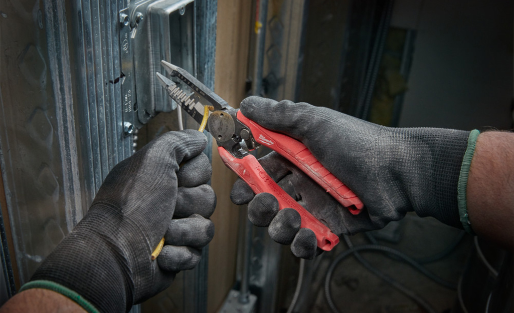 A person wearing work gloves uses a pair of electrician's pliers.
