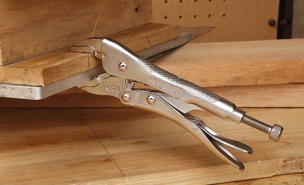 A pair of locking pliers is locked onto a piece of wood.