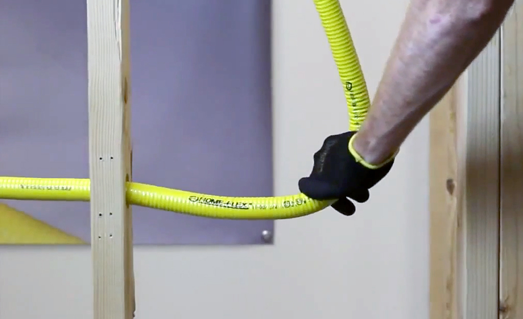 A person bends a section of CSST pipe between the studs of a building. 