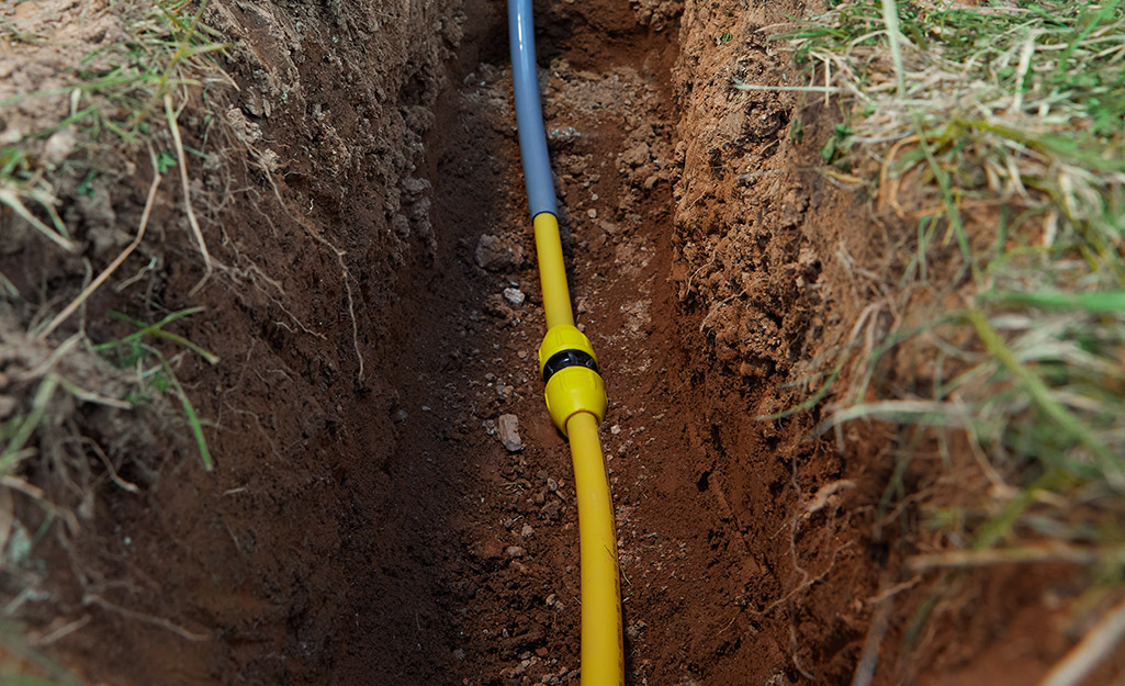 Polyethylene pipes lay at the bottom of a trench dug in a yard.