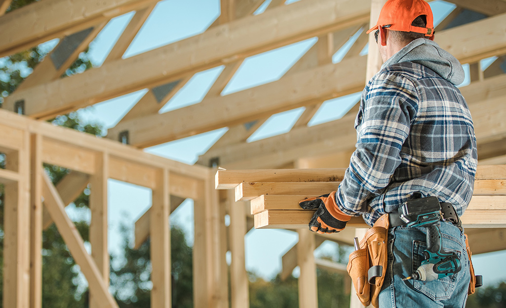 A construction worker carrying wood boards into a house frame.