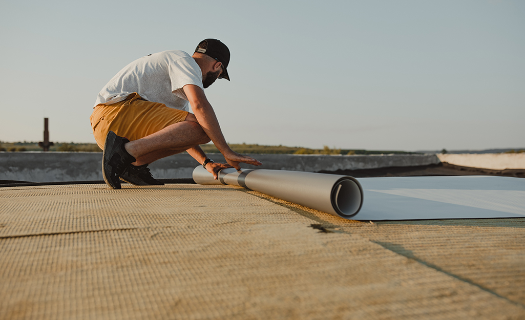A worker rolls out membrane roofing material.