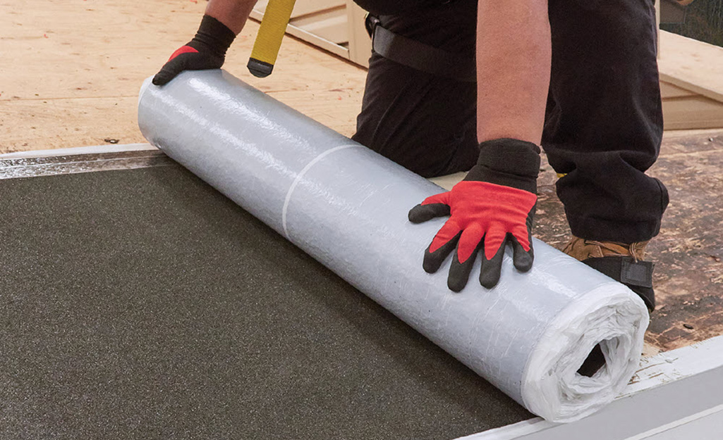 A worker applies rolled roofing material.