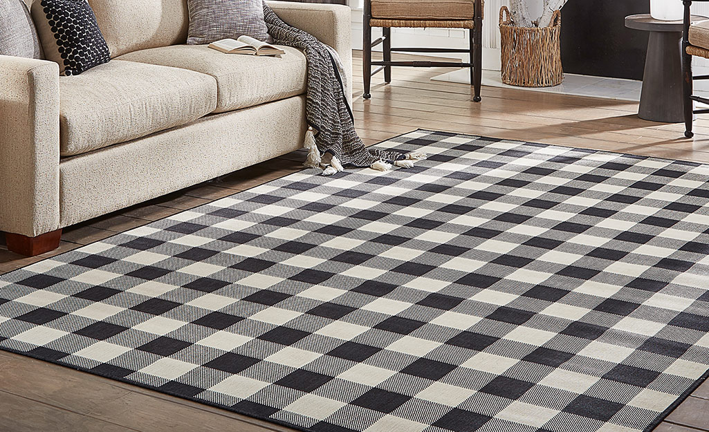 A black and white plaid rug lays in front of a couch.