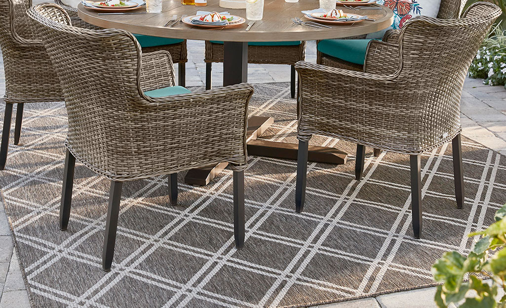 A synthetic rug lays under an outdoor dining set on a patio.