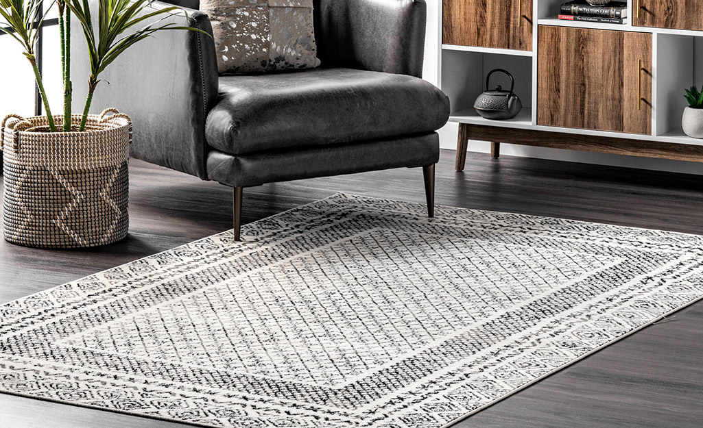 A border rug with gray patterns lays on the floor of a living room in front of an armchair.