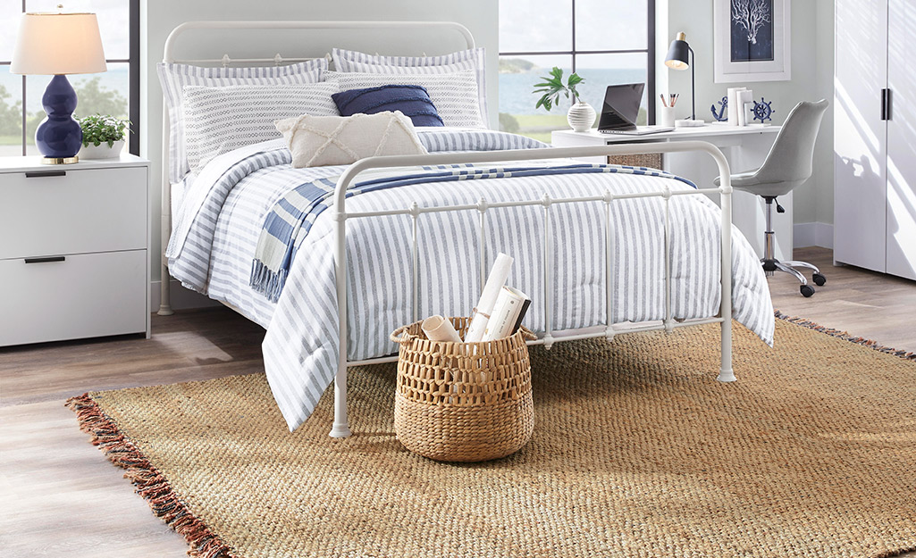  A coastal rug lays under an iron bed with navy and white bedding in a sunny bedroom.