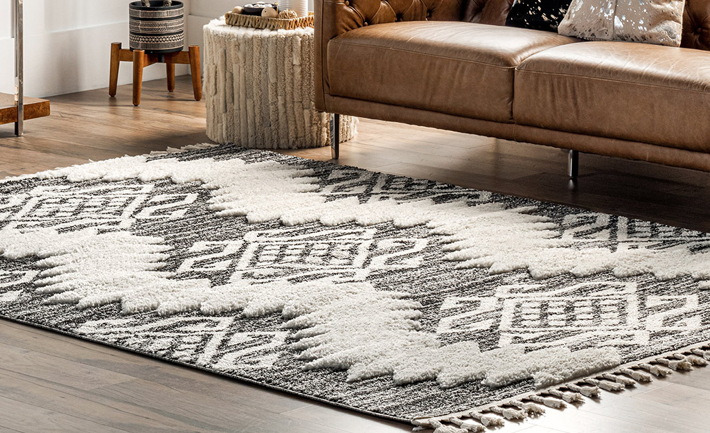 A high-low rug in gray and white lays in front of a couch in a living room.