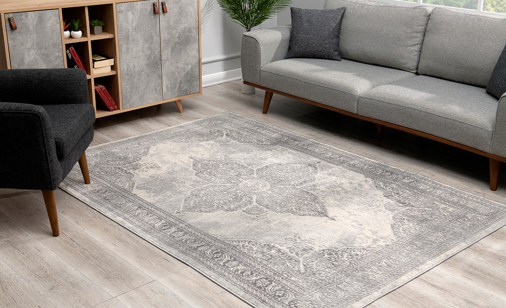 A distressed rug on a light grey floor positioned in front of a grey couch.
