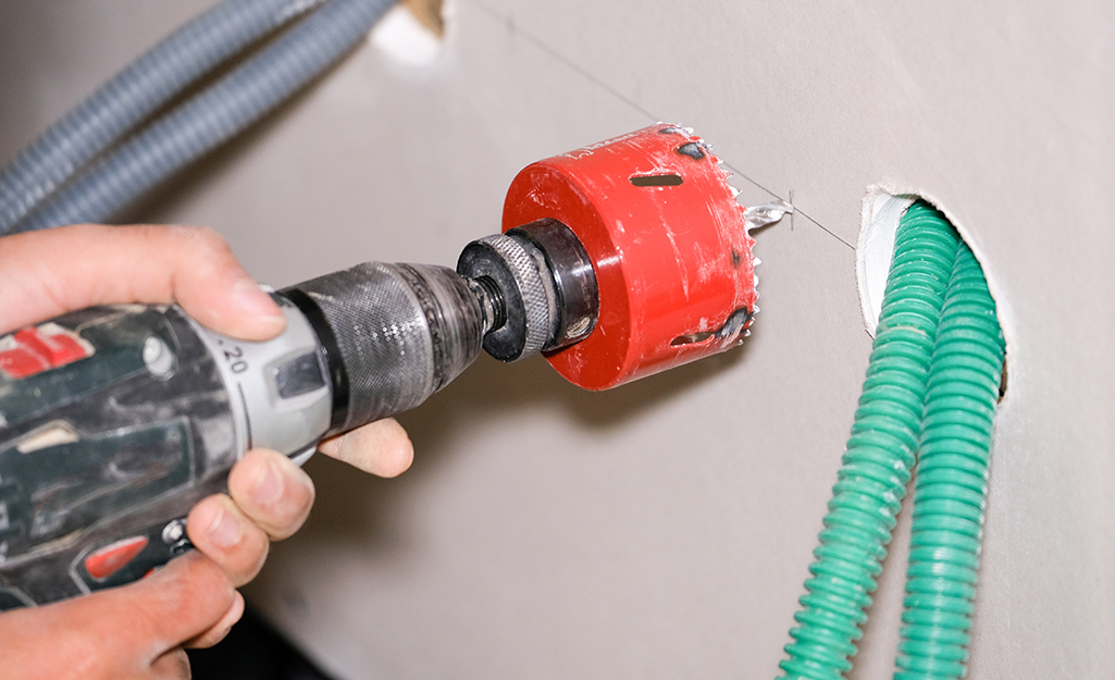 A person using a hole saw on drywall.