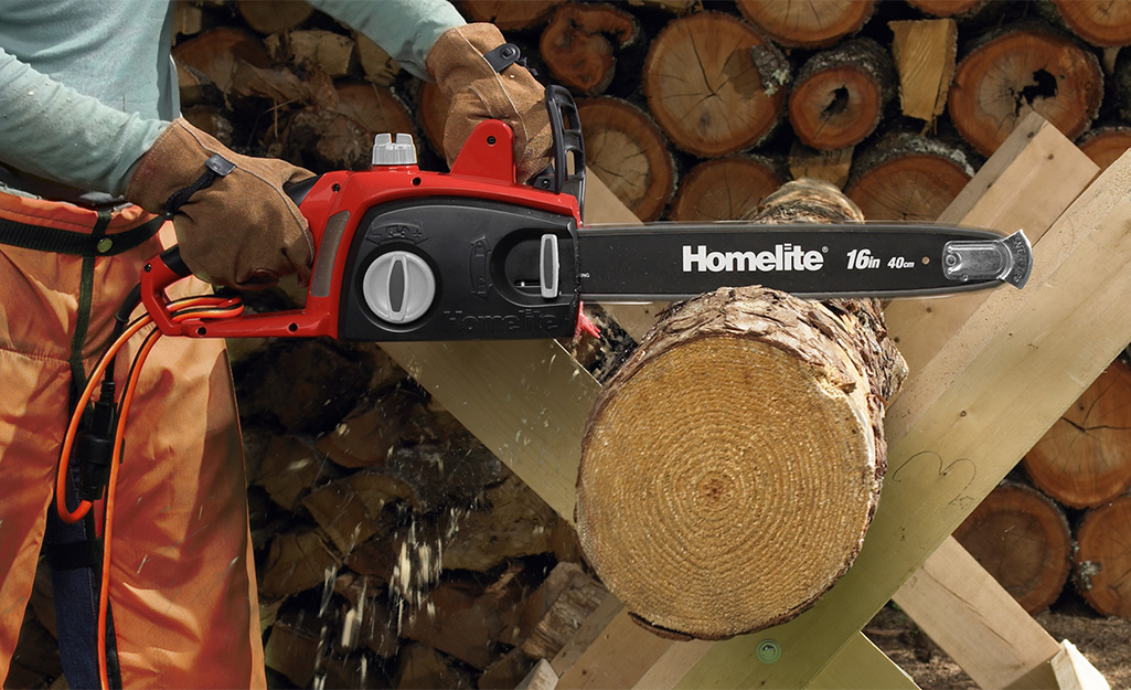 A person using a chainsaw to crosscut a tree section.