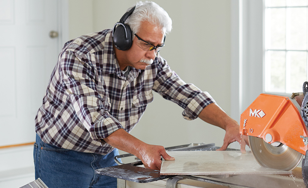 A person wears hearing protection to cut a board with a circular saw.