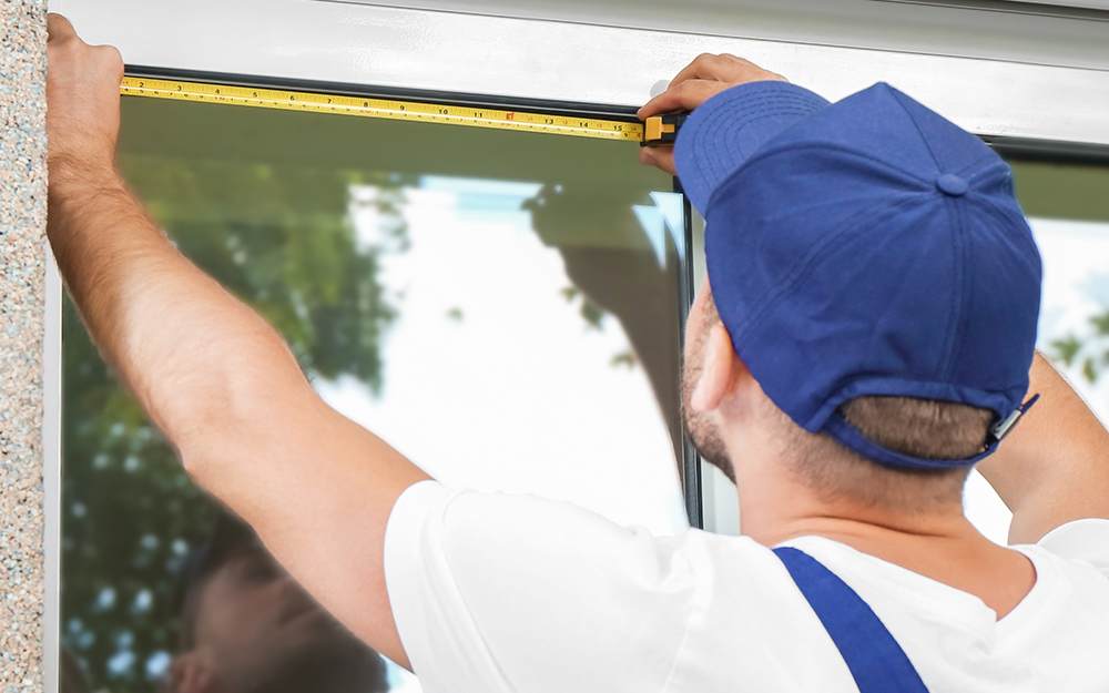 A worker in a blue hat measuring a window.