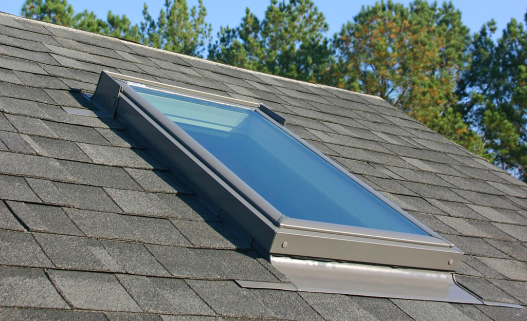 A skylight on the roof with dark shingles.