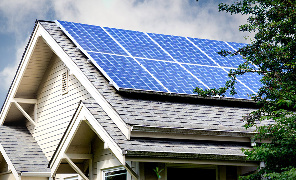 Solar panels cover most of the gray shingles on the sharply peaked roof of a house.