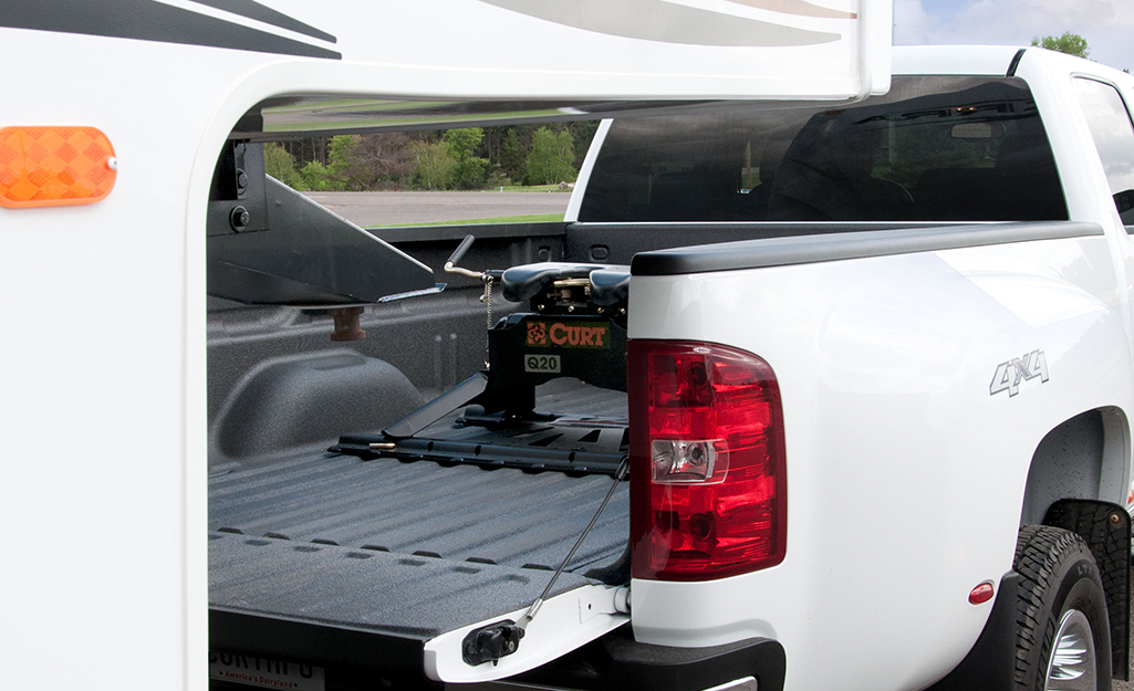 A gooseneck trailer connects to a gooseneck hitch in the back of a white pickup truck.
