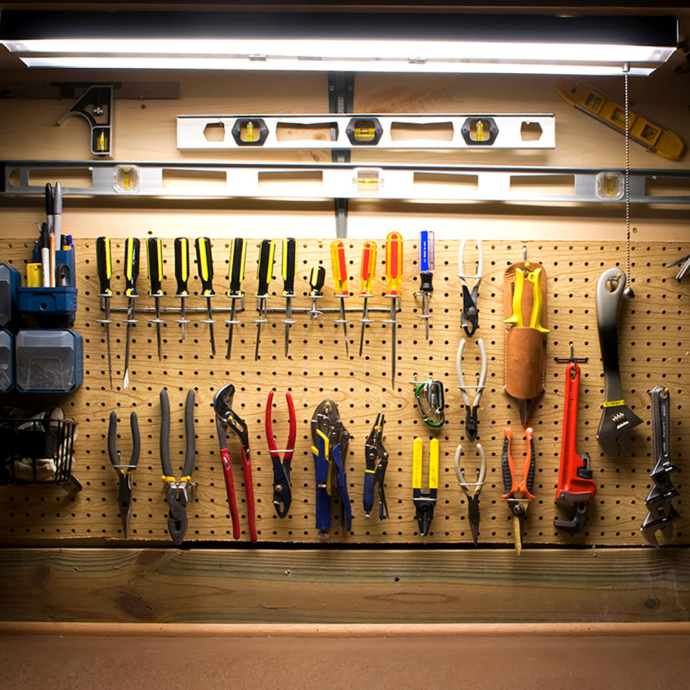 Tube lights hang over tools on a pegboard in a workshop.